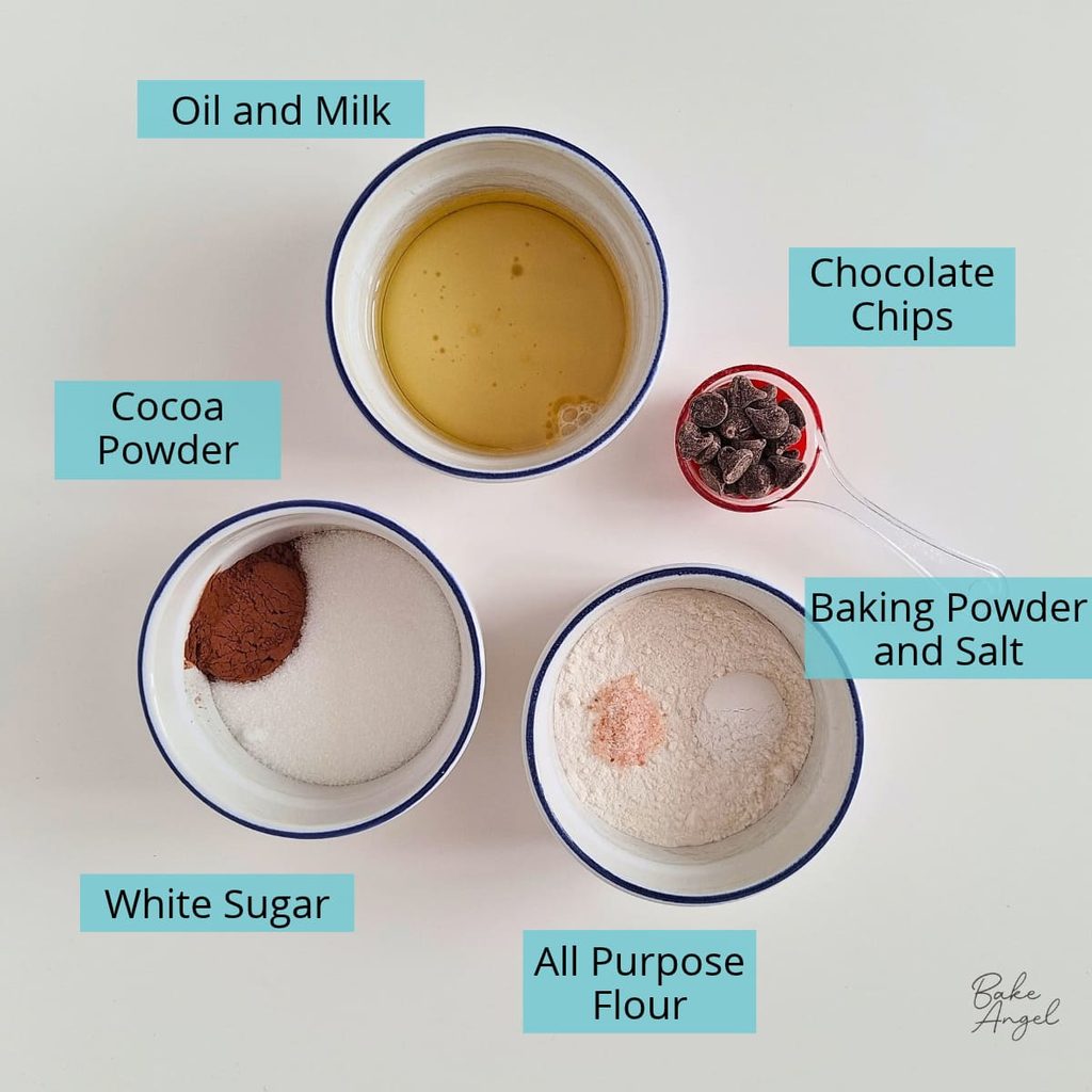 Ingredients measured out to make a vegan chocolate mug cake, including flour., cocoa powder, sugar, oil, plant based milk, and chocolate chips.