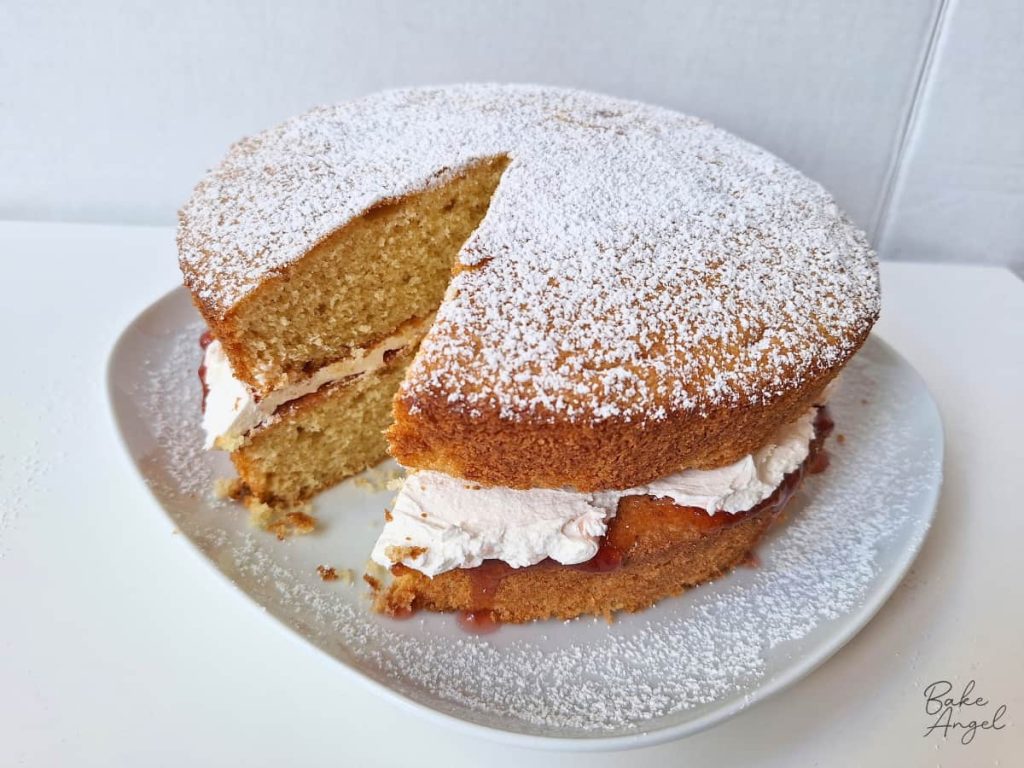 A bakery style Victoria sponge cake with a slice removed.