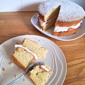 A slice of dairy-free gluten-free Victoria sponge cake on a plate, next to the whole cake.