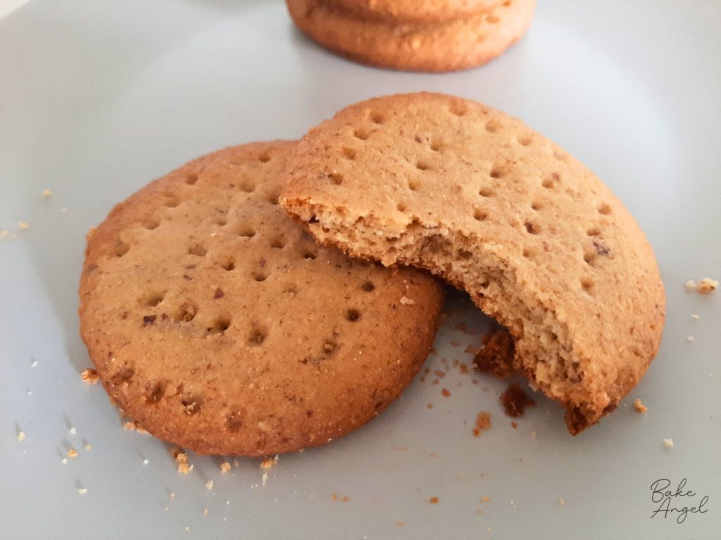 Two digestive biscuits on a plate with a bite taken out of one.