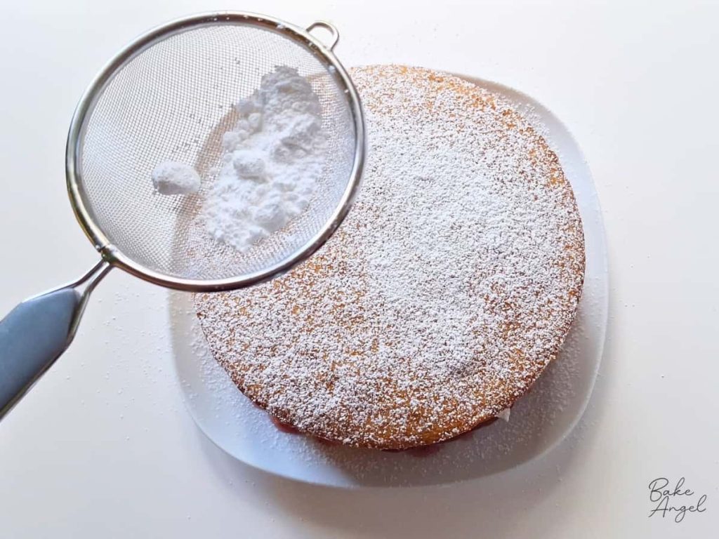 Icing sugar being dusted onto the top of a Victoria sponge cake, using a sieve.