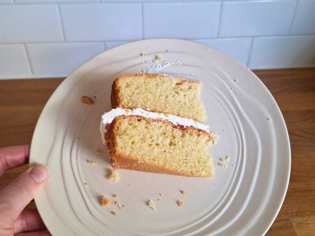 A slice of dairy-free gluten-free Victoria sponge cake on a cream coloured plate.