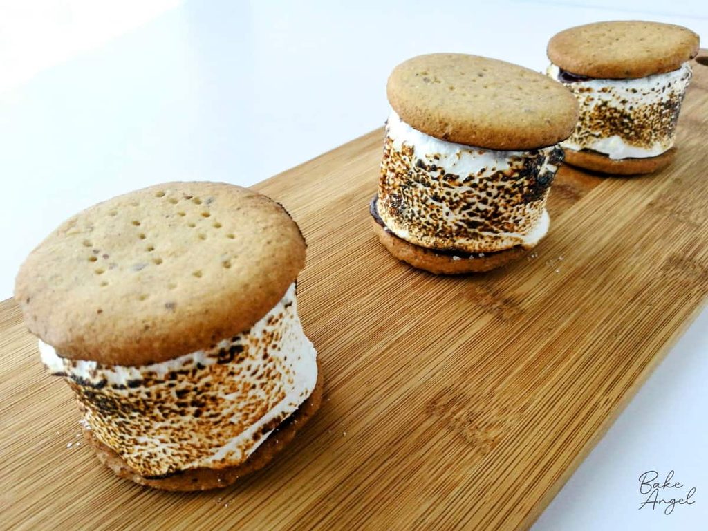 3 homemade s'mores on a wooden board, using torched marshmallows and homemade digestive biscuits.