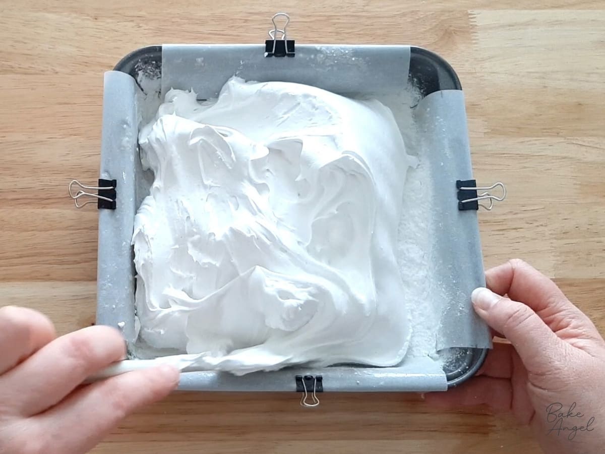 Using a spatula to spread the marshmallow mixture into the lined baking pan.