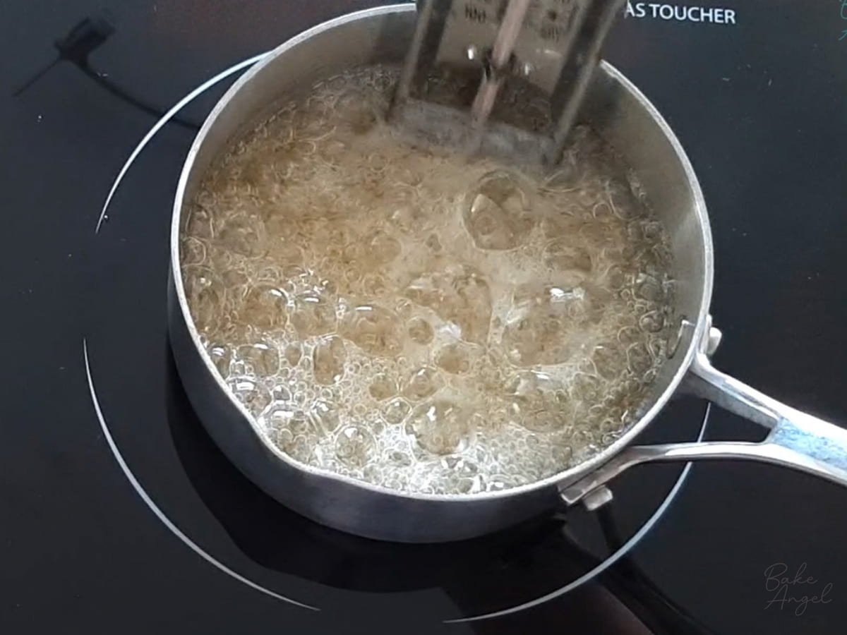 Sugar syrup boiling in a saucepan, with a candy thermometer.