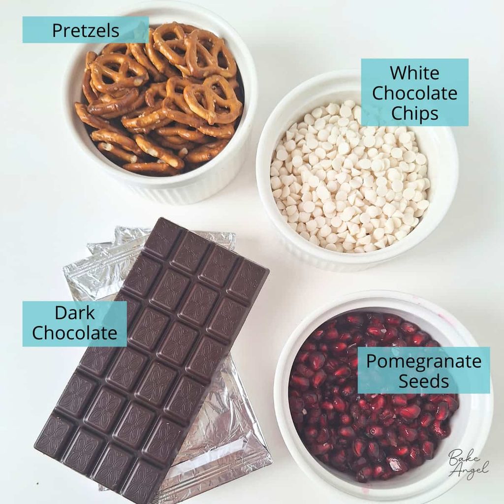 Pretzels, white chocolate chips, bars of dark chocolate, and pomegranate seeds measured out for making pretzel bark.