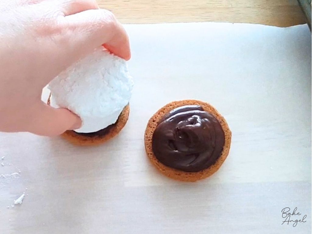 Placing a marshmallow on a chocolate covered digestive biscuit.