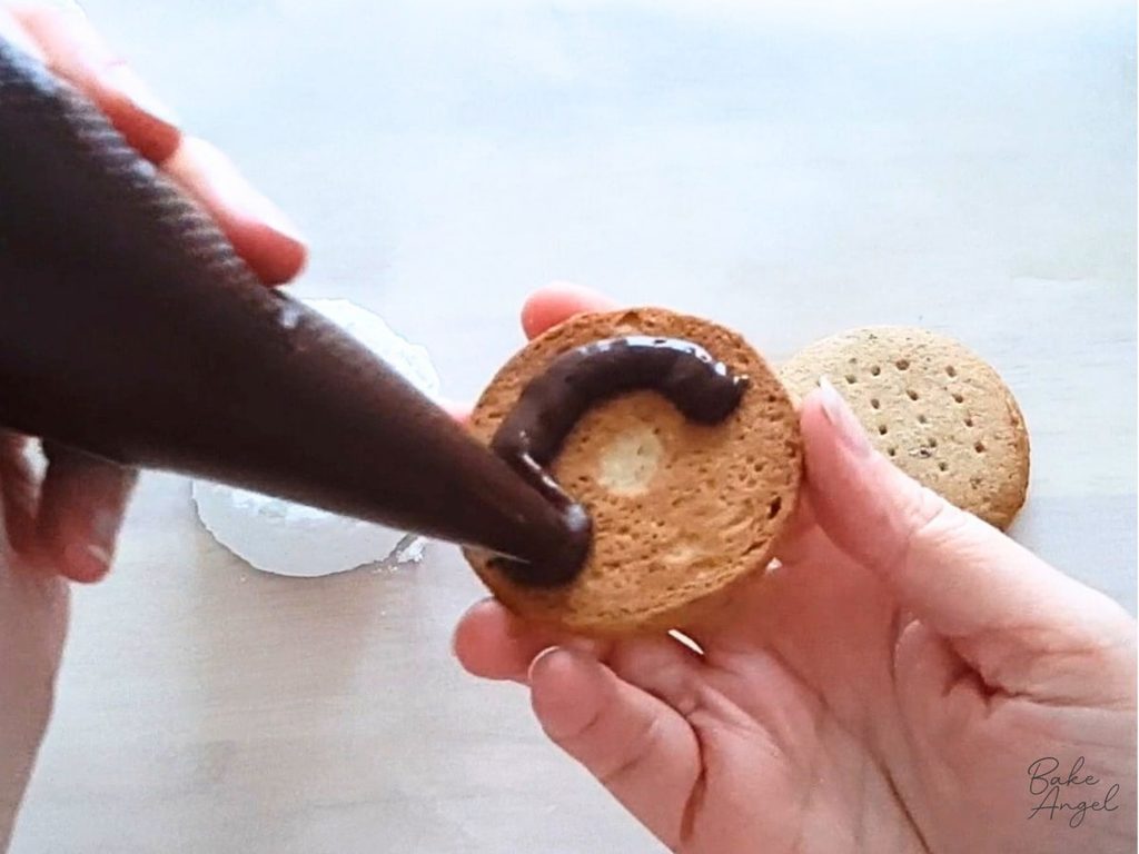 Piping a swirl of ganache onto the underside of a digestive biscuit.