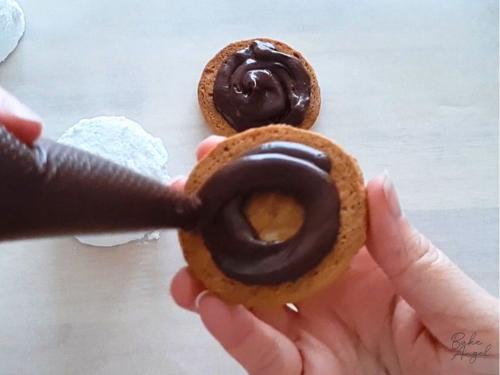 Piping a swirl of ganache onto the underside of a digestive biscuit.