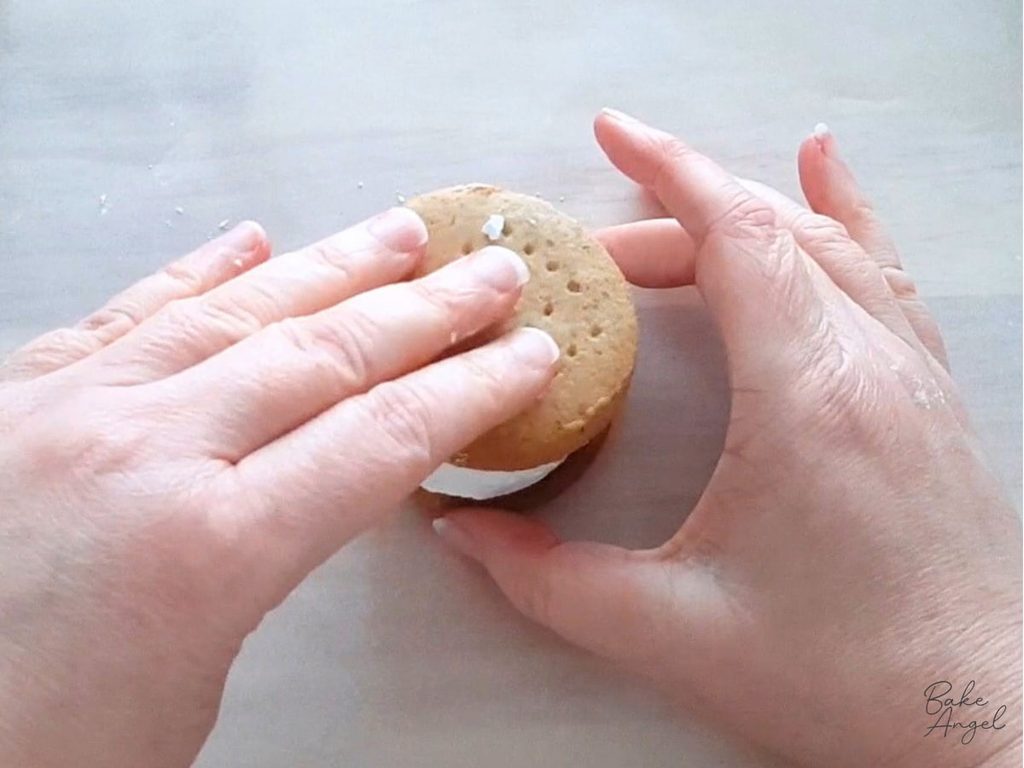 Pressing a biscuit on top of a marshmallow, while assembling a s'more.