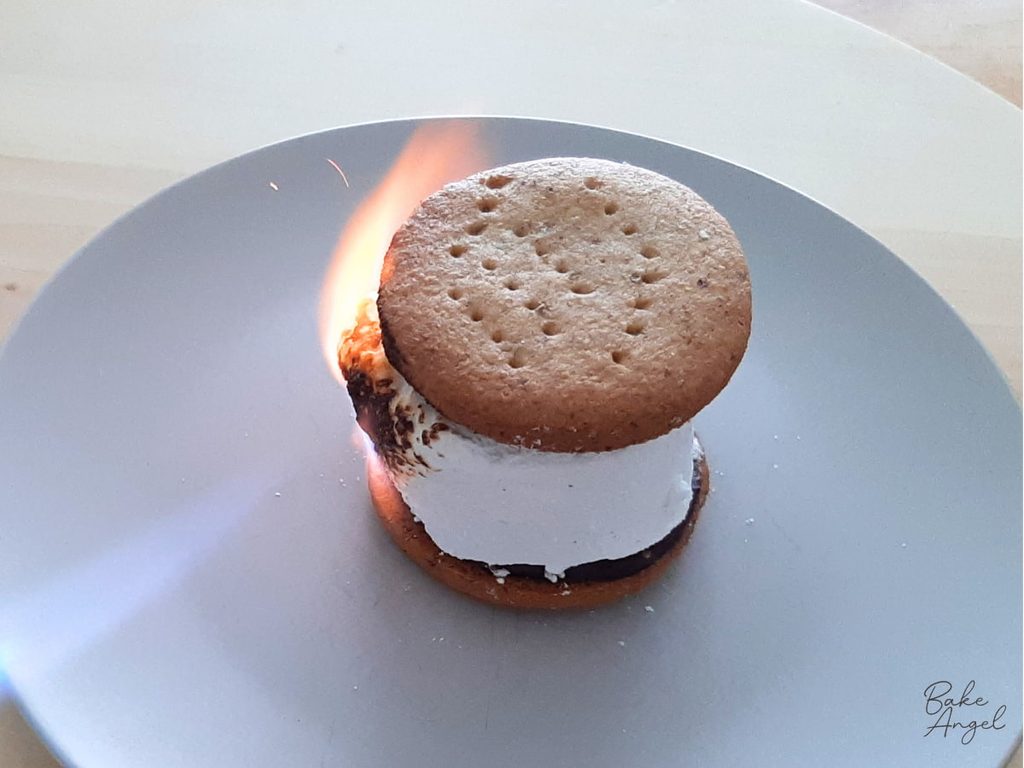 A large flame on the left side of a s'more, as the marshmallow is being toasted.